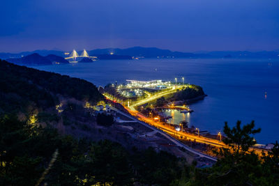 High angle view of illuminated city by sea at night