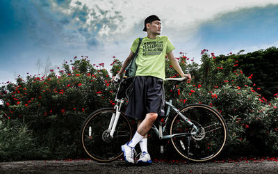 Low angle view of man standing with bicycle by flowering plants