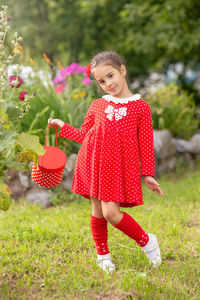 Portrait of a beautiful little girl in a red dress with polka dots, in a flower garden in summer.