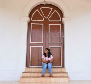 Full length of woman sitting at entrance of building