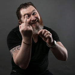 Mid adult man gesturing obscene gesture while sitting against black background