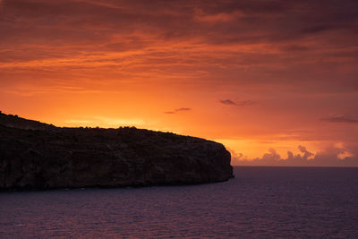 Rock by sea against sky during sunset