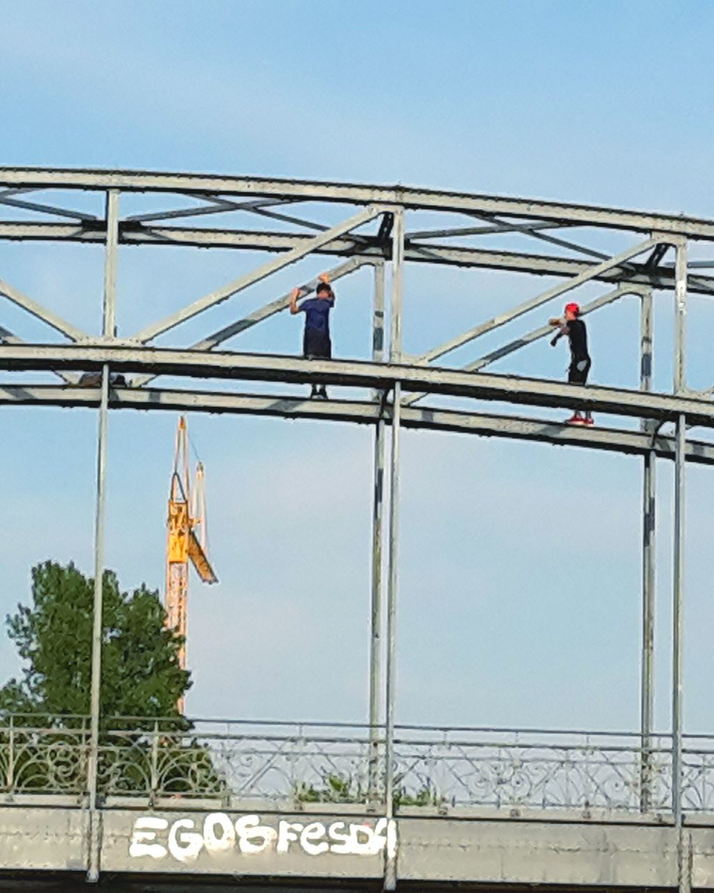 clear sky, low angle view, men, railing, connection, lifestyles, bridge - man made structure, built structure, leisure activity, transportation, standing, copy space, architecture, full length, sky, day, text, communication