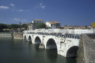 Bridge over river by buildings against blue sky