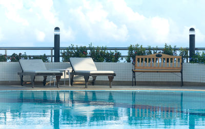 Chairs at swimming pool against sky