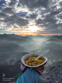 Person holding food against sky during sunset