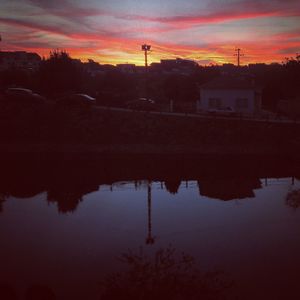 Reflection of silhouette trees in water against orange sky