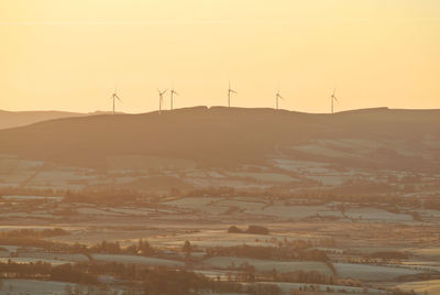 Wind turbines on a ridge silhouetted against an orange dawn sky