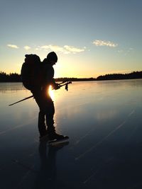 Silhouette man standing in lake against sky during sunset