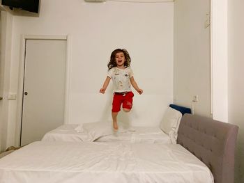 Full length of playful girl jumping on bed in bedroom