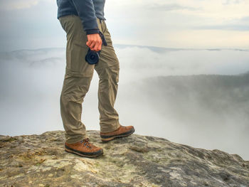 Low section of man standing on rock against sky