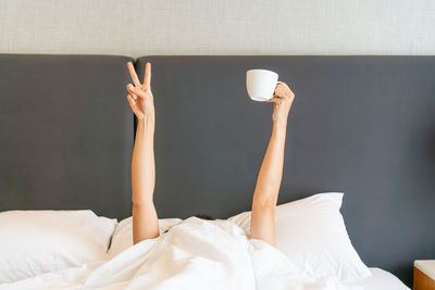 Woman stretching out her arms with a cup of coffee and showing v sign.