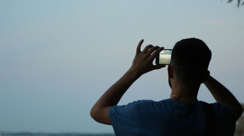 Rear view of man photographing against sky