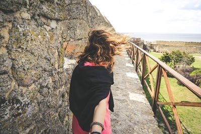 Rear view of woman standing on footpath against cloudy sky