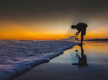 Silhouette man standing by sea against sky during sunset