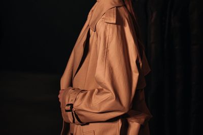 Young fashion model with cropped head in the stylish autumnal brown coat. indoor portrait