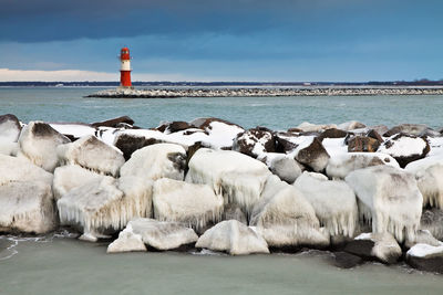 Frozen groyne on sea against cloudy sky