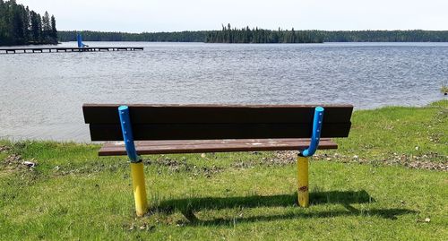 Empty bench on field by lake