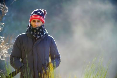 Portrait of man wearing warm clothing while standing on field during winter