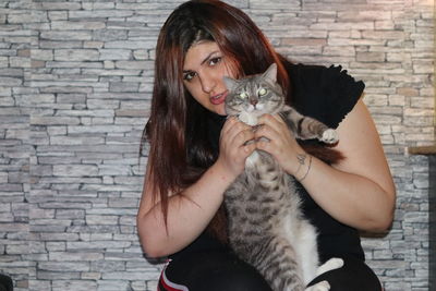 Portrait of woman holding cat against brick wall