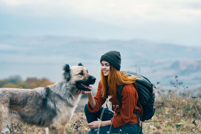 Young woman with dog standing against the sky