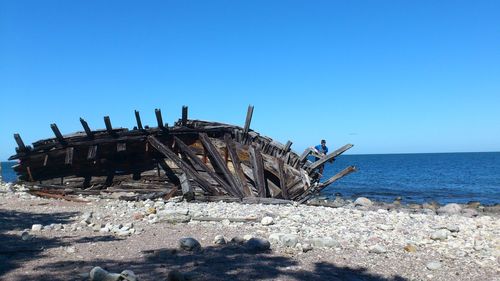 Man standing by shipwreck on sea shore against clear sky