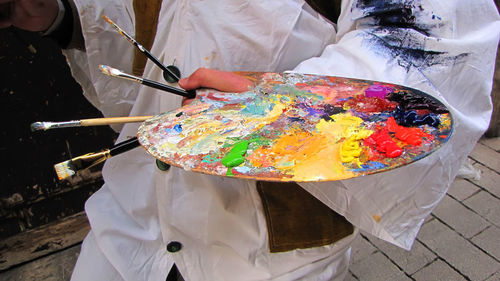 Close-up of hand holding painting brushes and messy palette