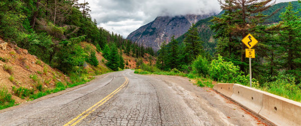 Empty road amidst trees against sky