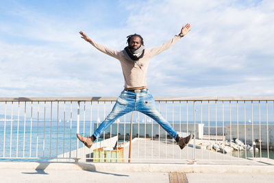 Full length of man jumping on railing against sky