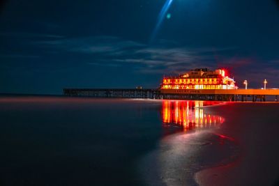 Illuminated building by sea against sky at night