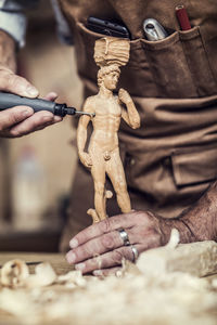 Midsection of carpenter carving on figurine in workshop