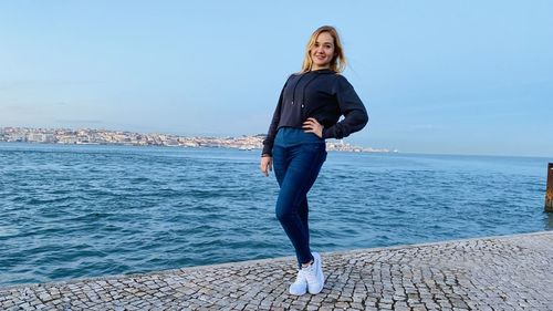 Full length portrait of young woman standing in sea against sky