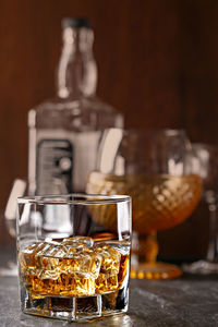 Ice cubes in glass of whiskey on table