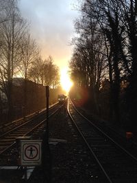 Railroad tracks amidst bare trees against sky during sunset