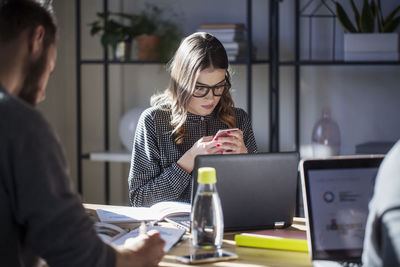 Woman using smart phone while sitting with friends in classroom