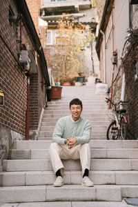 Portrait of smiling man sitting on staircase in city