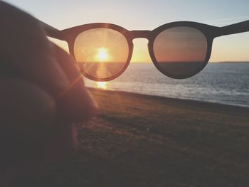 Close-up of hand by sea against sunset sky