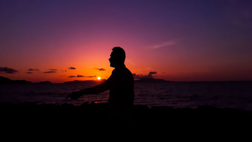 Silhouette man standing on beach against sky during sunset