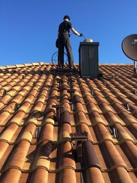 Low angle view of man standing on roof and cleaning the chimney 
