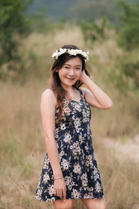 Portrait of smiling woman with hand in hair standing on field