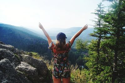 Rear view of woman with arms raised standing on mountain against sky