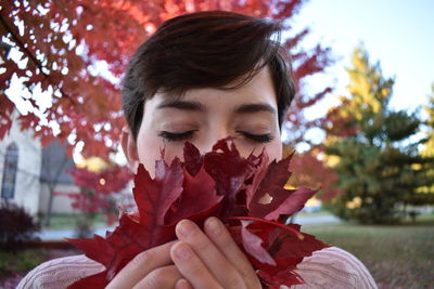 Close-up of young woman smelling fallen autumn leaves at park