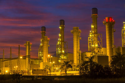 Illuminated factory against sky at sunset