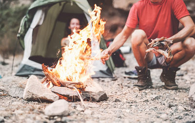 Low section of man by fire with woman sitting in tent