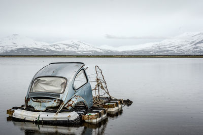 Abandoned vehicle part floating in lake against sky