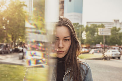 Portrait of beautiful young woman standing by glass in city