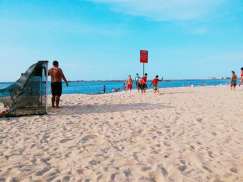 People playing soccer at beach against sky