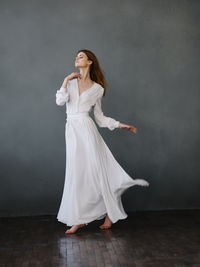 Young woman looking away while standing on floor against wall