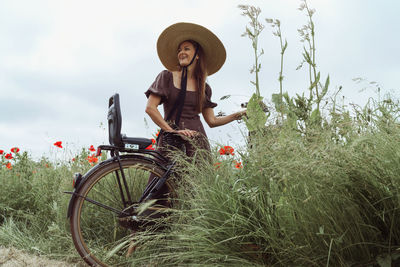 Portrait of young woman standing  on field with bicycle 