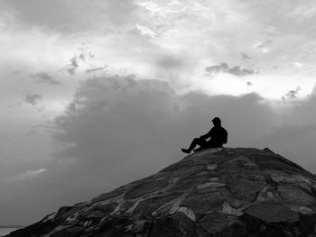 Silhouette man sitting on rock against sky